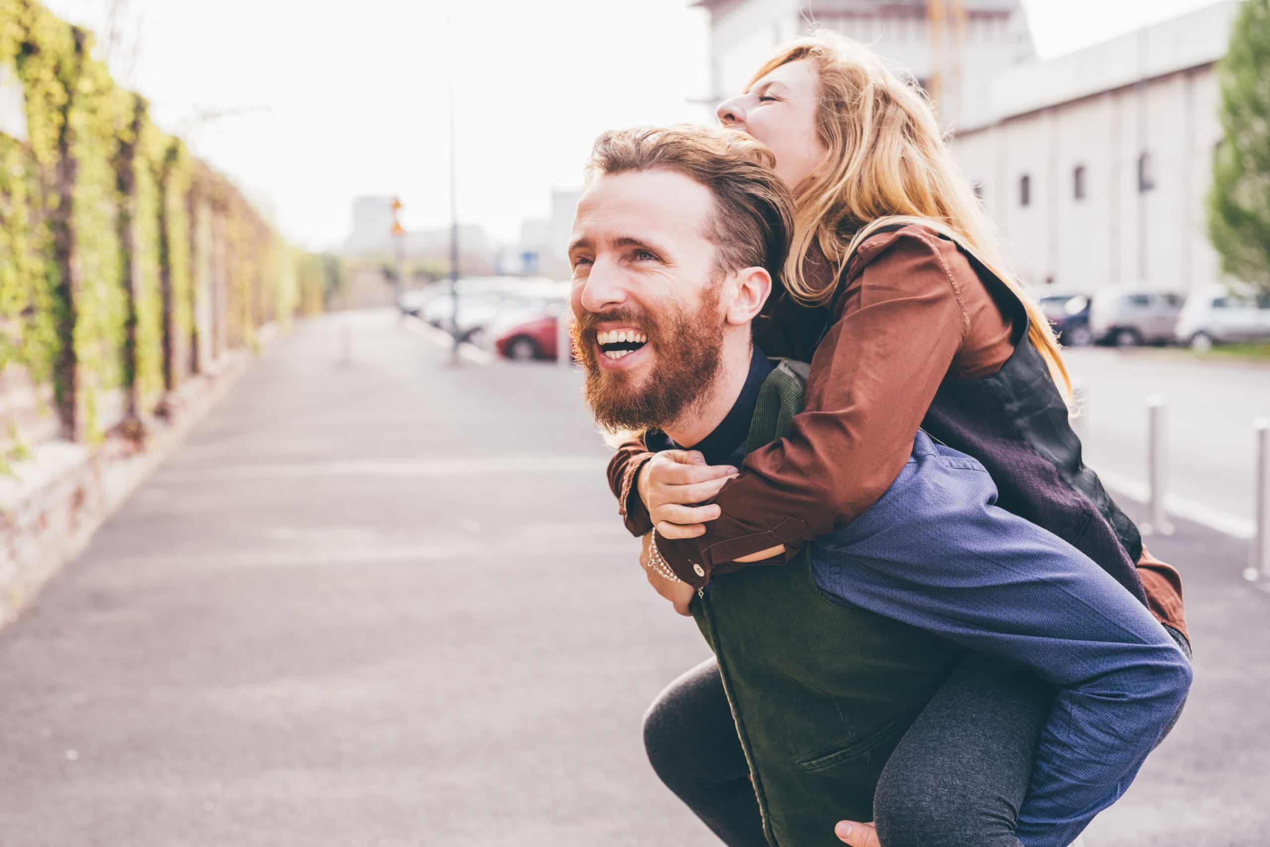 Couple of young beautiful redhead and blonde millennial woman and man, she is riding piggy back, both laughing - love, relationship, laughing concept